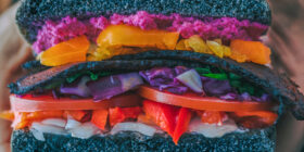 hands holding a sandwitch made with black bread and colorful fillings
