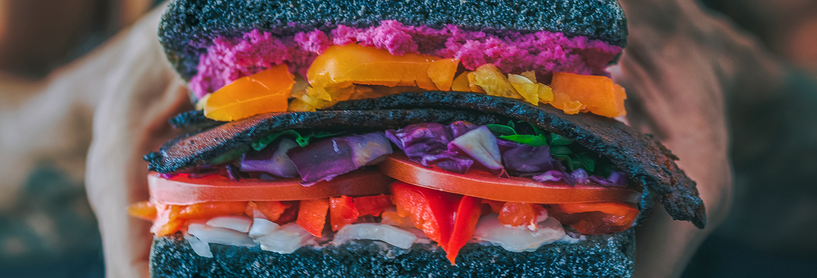 hands holding a sandwitch made with black bread and colorful fillings