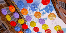 Looking up at many colorful umbrellas strung together between 2 buildings making a grid