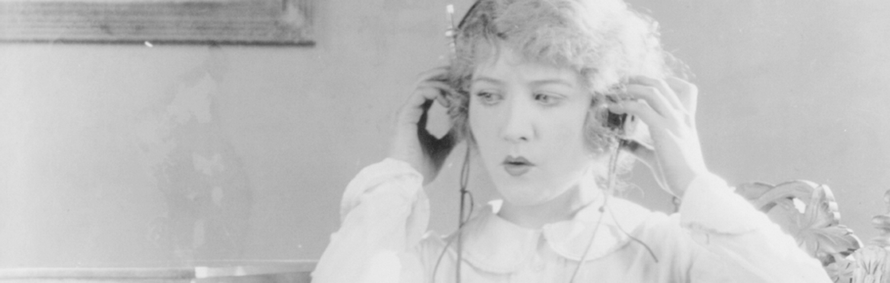 historic photograph shows women sitting next to radio listening to radio broadcast by holding headphones to ears.